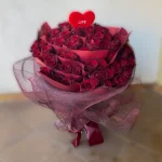 Wspaniały, okrągły bukiet ze 100 czerwonych róż oryginalnie przeplecionych czerwoną bibułą.