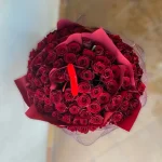 Wspaniały, okrągły bukiet ze 100 czerwonych róż oryginalnie przeplecionych czerwoną bibułą.