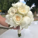 Elegancka kompozycja z białych róż i wonnych piwonii, idealna na uroczyste ceremonie. Czysta forma, subtelny wyraz, wykończona wstążką z perełkami.