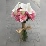 Okrągła wiązanka z białych lilii, otoczona różowymi goździkami symbolizującymi przywiązanie. Naturalny urok podkreśla sznurek otaczający łodygi.