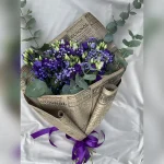 Wiązanka z eustomy, gipsówki i eukaliptusa w retro stylu, ozdobiona bibułą przypominającą stare gazety i fioletową kokardą – wyjątkowa i elegancka kompozycja.
