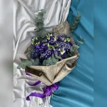 Wiązanka z eustomy, gipsówki i eukaliptusa w retro stylu, ozdobiona bibułą przypominającą stare gazety i fioletową kokardą – wyjątkowa i elegancka kompozycja.