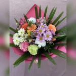 Kolorowy, radosny bukiet z róż, margaretek, goździków i tulipanów, ozdobiony baziami. Różowa bibuła i złoto-różowa wstążka dodają mu uroku.