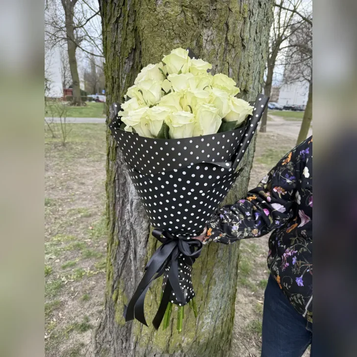 Wachlarzowo ułożone białe róże w czarnym rożku z bibuły w białe grochy, przewiązane czarną kokardą – elegancka, leżąca kompozycja kwiatowa.