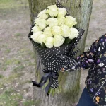 Wachlarzowo ułożone białe róże w czarnym rożku z bibuły w białe grochy, przewiązane czarną kokardą – elegancka, leżąca kompozycja kwiatowa.