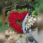 Wieniec pogrzebowy w kształcie serca z czerwonych róż, ozdobiony białymi liliami, czarną kokardą i gałązkami ostrokrzewu, wykonany w Kwiaciarni Klara.