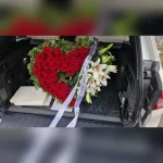Wieniec pogrzebowy w kształcie serca z czerwonych róż, ozdobiony białymi liliami, czarną kokardą i gałązkami ostrokrzewu, wykonany w Kwiaciarni Klara.