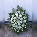 Wieniec z Kwiaciarni Klara, składający się z białych lilii i róż, z pąkami białych róż przeplecionymi gałązkami paproci, tworzący koronkową ramę, podkreślającą biel kwiatów.